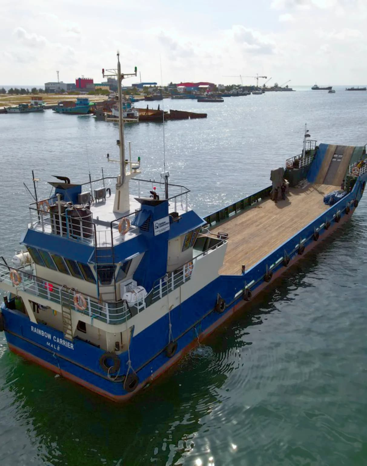 Rainbow's landing craft with its cargo deck, moored in a harbour.