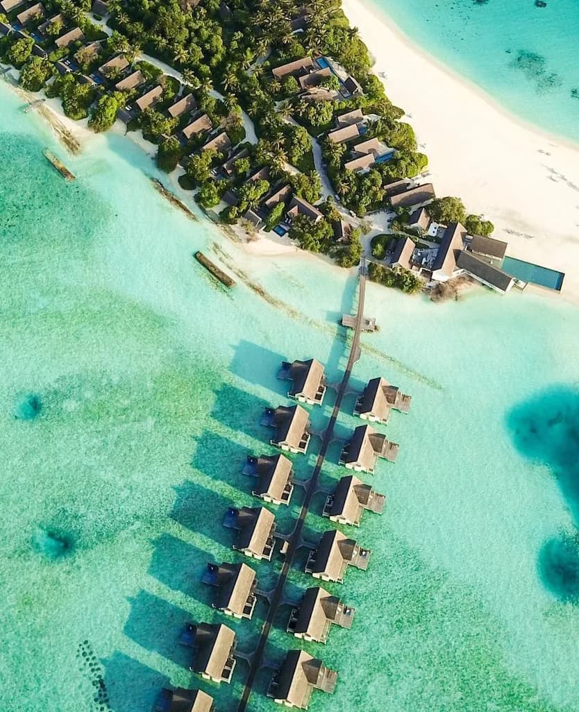 Aerial photograph of a Maldives resort: over-water villas along a jetty off a wooded island.